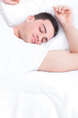Fototapeta na wymiar Handsome young man happily sleeping in white bed