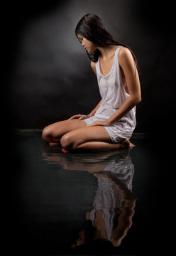 Girl in a white shirt sitting in water on a black background.
