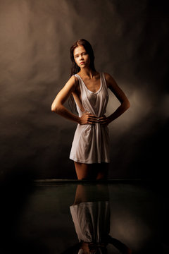 Girl in a white shirt standing in water on a black background.