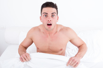 shocked half naked young man in bed  looking down at his underwe