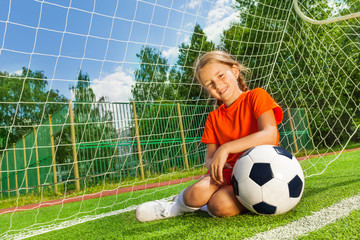 Smiling girl with bending arm on football sitting