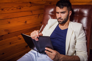 Handsome young man in white suit relaxing on luxury sofa with di