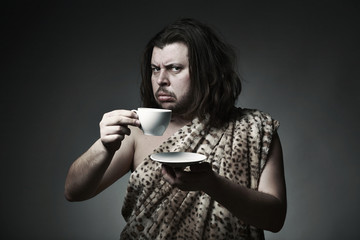 Savage man in skin of beast drink tea or coffee - obrazy, fototapety, plakaty
