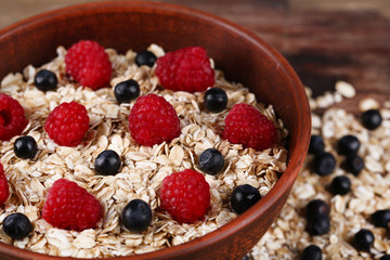 Big brown bowl with oatmeal and berries on a wooden table