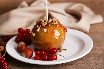 Sweet caramel apple on stick with berries, on wooden table