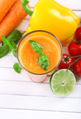 Glass of fresh carrot juice and vegetables on wooden background