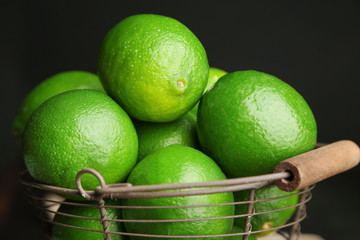 Fresh juicy limes in basket on wooden table, on dark background