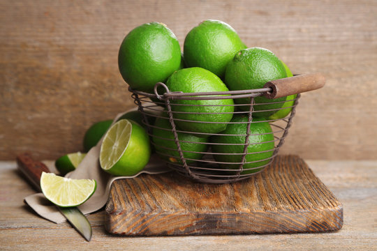 Fresh juicy limes in basket on old wooden background