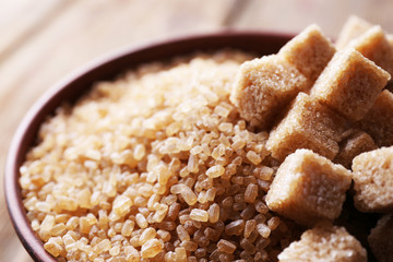 Brown sugar cubes and crystal sugar in bowl on wooden