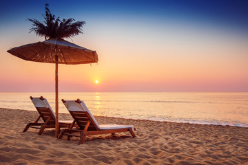 Vivid sunrise on a beautiful sandy beach with sunshade - obrazy, fototapety, plakaty