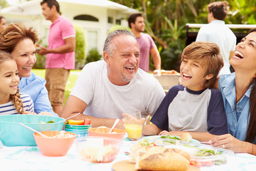 Multi Generation Family Enjoying Meal In Garden Together