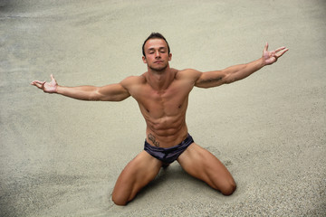 Fit young bodybuilder on the beach, arms spread open