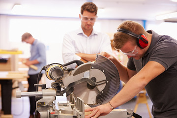 Student And Teacher In Carpentry Class Using Circular Saw