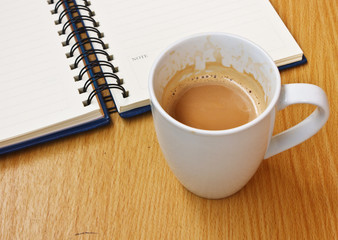 White cup of hot coffee and Notebook on wood table