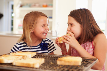 Two Girls Eating Cheese On Toast In Kitchen