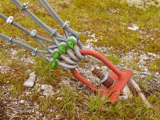 Detail of red iron hanger anchored into ground, twisted ropes