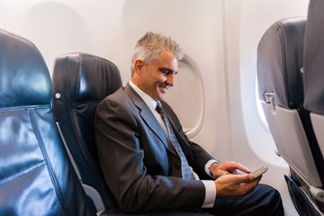 middle aged businessman using cell phone on airplane
