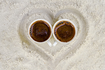 two cups with hot coffee on sand