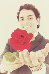 smiling man in a suit holding a red rose and offers it to the ca