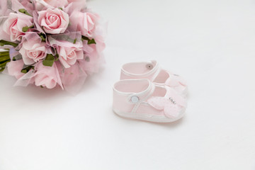 Fototapeta na wymiar Pink flowers and children's sandals on the white bed