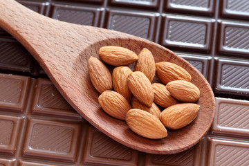 Almonds in a wooden spoon on chocolate background