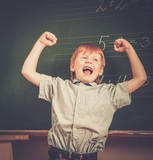 Little funny redhead schoolboy near blackboard