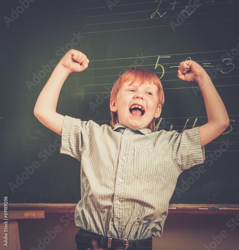 Little funny redhead schoolboy near blackboard