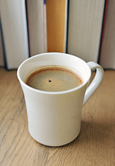 Freshly brewed coffee cup against books.