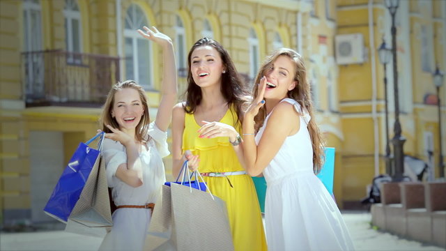 Three girls waving and attract attention holding shopping bags