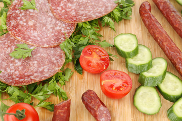 Sausage salami and vegetables on wooden platter.