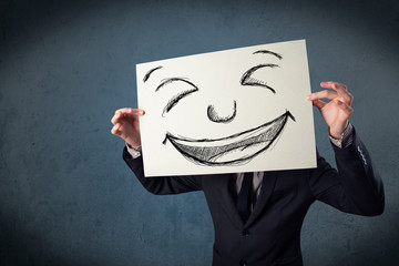 Businessman holding a paper with smiley face in front of his hea