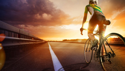 Cyclist riding a bike on an open road to the sunset