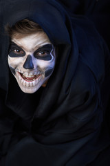 Teen with make-up of skull in black cloak laughs