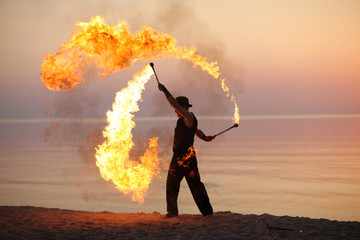 Professional fire juggler performing on the beach - obrazy, fototapety, plakaty