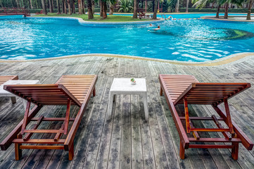 Wooden sunbath chair and side table in luxury swimming pool