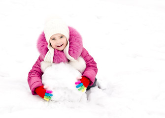 Cute smiling little girl makes snowman in winter day