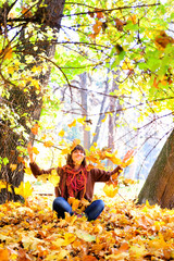 Woman throws autumn leaves in park.