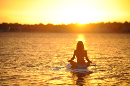 Frau meditiert auf einem Stand Up Paddle Board bei Sonnenaufgang