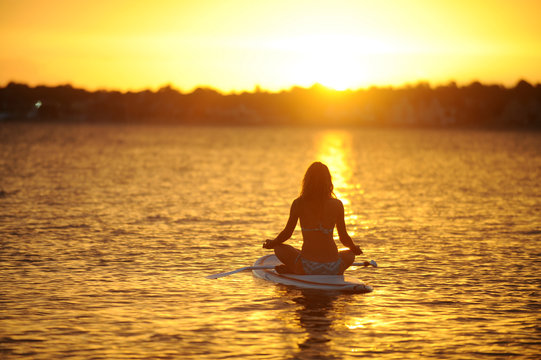 Frau  meditiert auf Surfboard im See