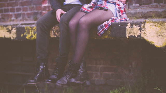 Guy and girl sitting on ledge with boots dangling from it