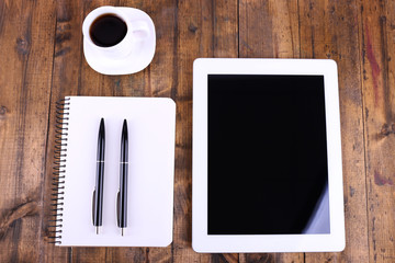 Tablet, cup of coffee, notebook and pens on wooden background