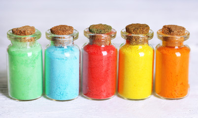 Bottles with colorful dry pigments on wooden background