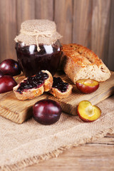 Tasty plum jam in jar and plums on wooden table close-up