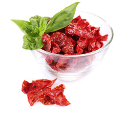 Sun dried tomatoes in glass bowl and basil leaves, isolated