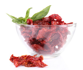 Sun dried tomatoes in glass bowl and basil leaves, isolated