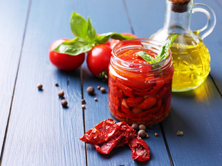 Sun dried tomatoes in glass jar on color wooden background