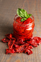 Sun dried tomatoes in glass jar, basil leaves