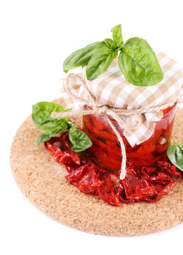 Sun dried tomatoes in glass jar and basil leaves isolated