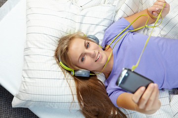 Blonde woman lying on bed while listening music through headphon