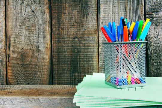 Pens and writing-books on a wooden shelf.